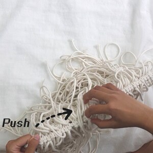 May include: A close-up of a hand pushing a bundle of white cotton rope together. The rope is knotted and has a fringe at the bottom. The text "Push" is written on the image.