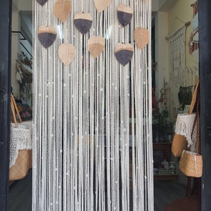 May include: A white macrame wall hanging with a geometric pattern and brown and gray leaf-shaped accents.
