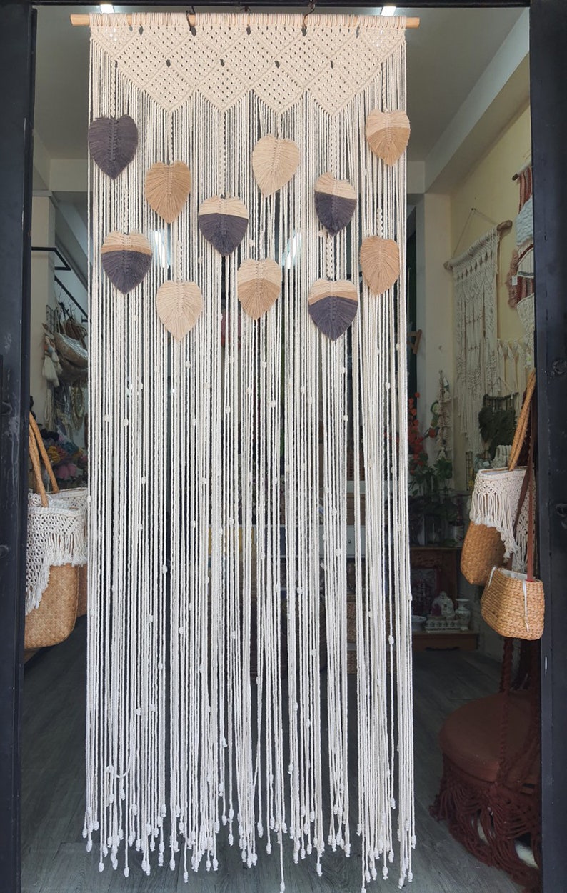 May include: A white macrame wall hanging with a geometric pattern and brown and gray leaf-shaped accents.