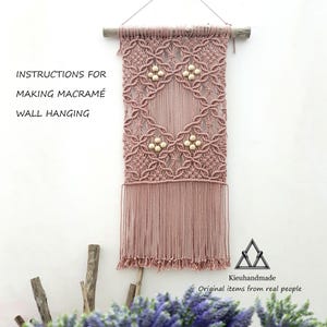 May include: A dusty rose macramé wall hanging with a geometric design and wooden beads. The wall hanging is suspended from a wooden dowel and features long fringe at the bottom. Text on the image reads "Instructions for Making Macramé Wall Hanging."