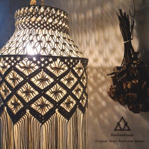 Puede incluir: Una pantalla de lámpara de macramé beige y marrón hecha a mano con un diseño geométrico y flecos. La imagen también muestra flores secas y el texto "Kieuhandmade Original items from real people."