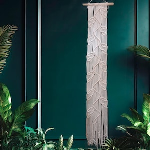 May include: A white macrame wall hanging with a leaf pattern against a teal green wall.