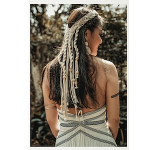 May include: A woman with long dark hair wearing a white crochet halter top with black trim and a white crochet headband with wooden beads.