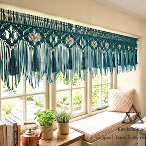 May include: A teal macrame window valance featuring intricate knotted patterns, hanging wooden beads, and long fringe tassels. The valance is suspended from a silver curtain rod and displays a repeating geometric design across the top section.
