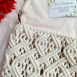 May include: A white macrame bag with a knotted design. The bag has a white strap with a silver clasp.