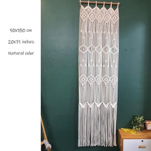 May include: A white macrame wall hanging with a geometric pattern. It measures 50x180 cm or 20x71 inches. The wall hanging is made of natural cotton cord and has a natural color.