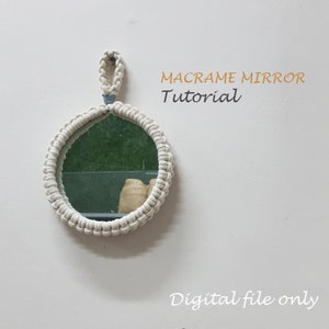 以下が含まれることがあります： 白いマクラメの鏡で、吊り下げ用のループが付いています。鏡は丸く、シンプルなデザインです。鏡の上にオレンジ色の文字で「MACRAME MIRROR Tutorial」と書いてあります。鏡の下に黒い文字で「Digital file only」と書いてあります。