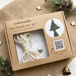 May include: A brown cardboard box for a macrame DIY kit featuring the text Kieuhandmudeshop MACRAME DIY KIT CHRISTMAS ORNAMENT. The box has a window showing a coil of off-white cord, a printed image of a green tree ornament, and a QR code.