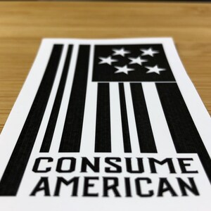 May include: Black and white sticker with a stylised American flag design and the text "CONSUME AMERICAN".