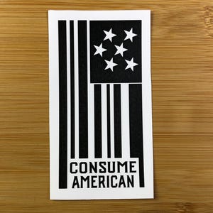 May include: Black and white sticker with a stylized American flag design and the text "CONSUME AMERICAN".