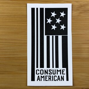 May include: Black and white sticker with a stylized American flag and the text "CONSUME AMERICAN".