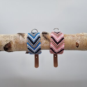 May include: Two dog collars with chevron patterns. One collar is blue, white and black. The other collar is pink, white and black. Both collars have brown leather straps.