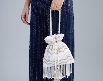 May include: White drawstring bag with gold and silver embroidery. The bag has a beaded handle and a long beaded tassel. The bag is held against a dark blue sequined jumpsuit.