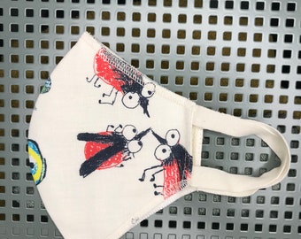 May include: White cotton face mask with red and black bug illustrations. The mask has adjustable ear loops.