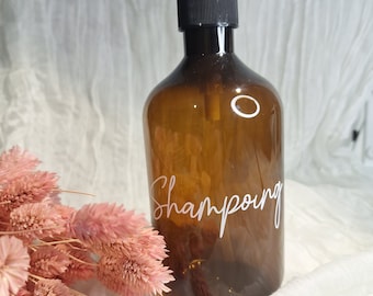 May include: A brown glass bottle with a black pump dispenser and a white label that says "Shampoing".