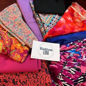 May include: A collection of colorful fabric scraps, including paisley, floral, and geometric patterns. The fabrics are arranged in a pile, with a white card that reads "Button Loni Handmade in USA" at the bottom.