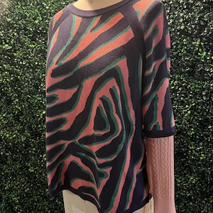 May include: A navy blue, pink, and green patterned sweater with a pink cable knit cuff. The sweater has a round neckline and a relaxed fit.