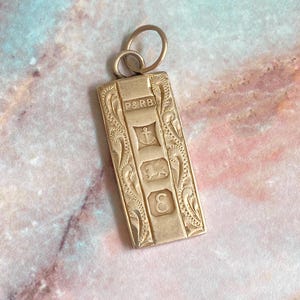 May include: A rectangular gold pendant featuring an engraved scrollwork border and a central vertical panel. The panel displays the text P&RB above three distinct hallmarks, including an anchor, a lion, and the letter E, with a circular jump ring.