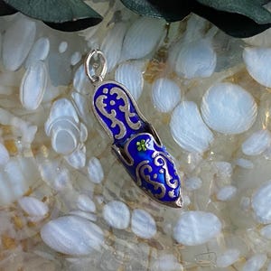 Può includere: Un ciondolo d'argento a forma di pantofola blu con un design a filigrana argentata. La pantofola ha una pietra preziosa verde sulla parte superiore.