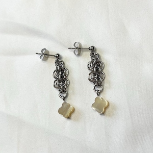 Puede incluir: Un par de pendientes de plata con un diseño de cadena y un dije de flor de concha blanca.