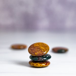 May include: A stack of three round, polished stones. The top stone is a mix of red, yellow, and brown. The middle stone is green and blue. The bottom stone is yellow and brown.