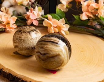 May include: Two decorative spheres made of brown and white striped agate. The spheres are sitting on a wooden surface.