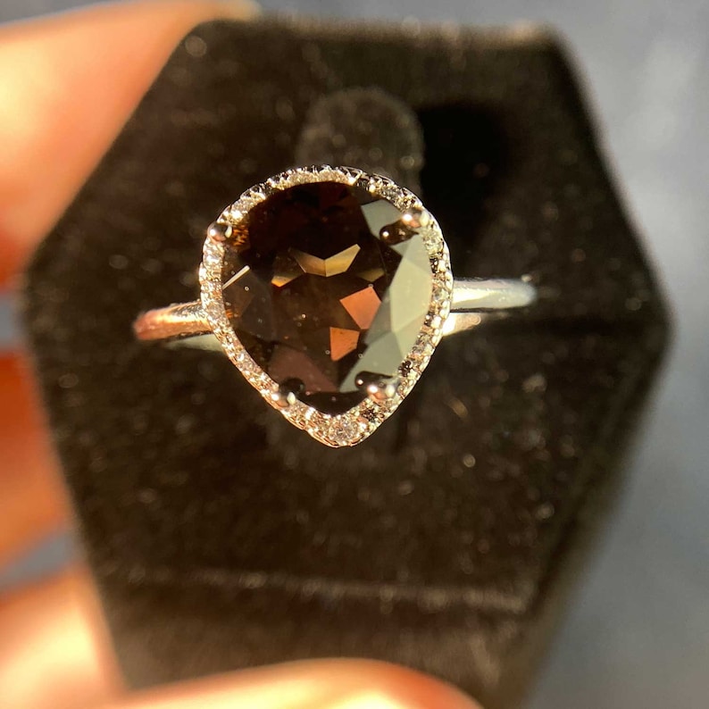 May include: A pear-shaped brown gemstone ring with a halo of small diamonds set in silver.
