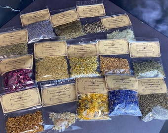 May include: Assortment of dried herbs and flowers in clear plastic bags with brown paper labels. The labels list the names of the herbs and flowers, such as "Lemon Verbena", "Elderflowers", "Chamomile Flowers", "Rosemary Leaf", "Calendula Flowers", "Orange Peel", "Frankincense Resin", and "Peppermint Leaf".
