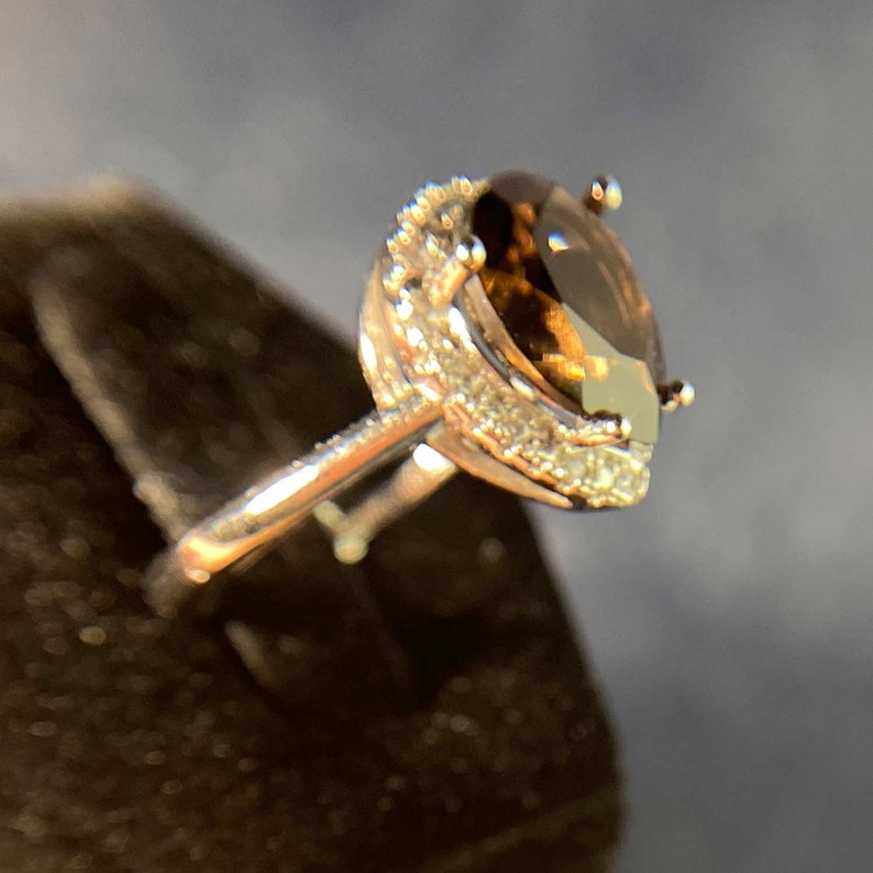May include: A silver ring with a large, oval-shaped, brown gemstone surrounded by a halo of smaller, white gemstones.