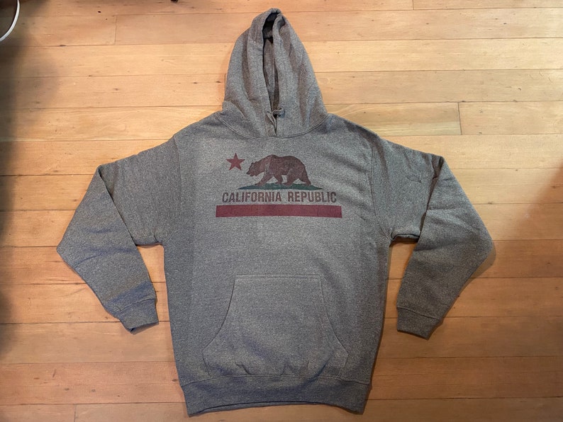 May include: A gray hooded sweatshirt with a vintage-style California Republic graphic featuring a brown bear and a red star. The graphic also includes the text "CALIFORNIA REPUBLIC" in red.