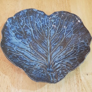 Puede incluir: Un plato para servir de cerámica azul y blanco con forma de hoja de col.