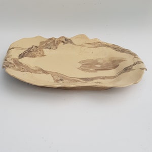 Puede incluir: Una fuente de cerámica oblonga hecha a mano. La superficie beige presenta vetas marrones, creando una estética natural y orgánica. Los bordes tienen una forma ligeramente irregular y ondulada, añadiendo carácter.