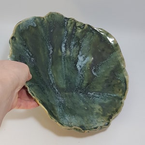 Puede incluir: Un cuenco de cerámica verde con una forma ondulada y orgánica. El cuenco tiene un esmalte verde claro con un efecto de mármol blanco.