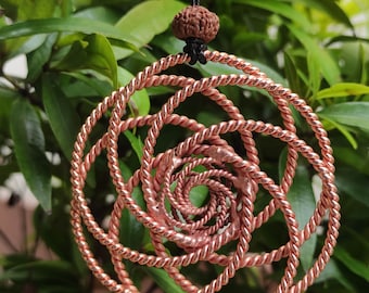 May include: A copper wire spiral pendant with a brown bead at the top, hanging from a black cord. The pendant is a series of concentric circles, each with a twisted wire design.