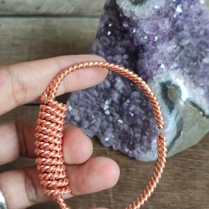 Puede incluir: Un brazalete de alambre de cobre con un diseño trenzado. El brazalete está enrollado en forma de espiral.