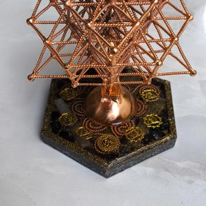 Może przedstawiać: Miedziana rzeźba geometryczna o skomplikowanym, ażurowym wzorze. Rzeźba stoi na sześciokątnej podstawie ze złotymi zdobieniami i czarno-złotą obwódką. Całość jest skomplikowana i artystyczna.