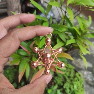 May include: A copper wire and crystal pendant in the shape of a star with a clear crystal in the center. The pendant is held in a hand.