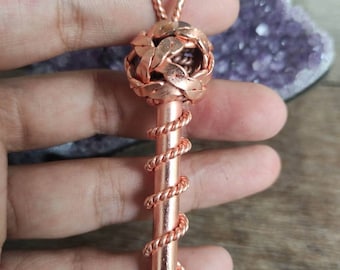 May include: A copper-colored pendant in the shape of a key. The top of the key features a woven sphere design, while the stem is wrapped with a spiral of copper wire. The key is suspended from a looped bail.