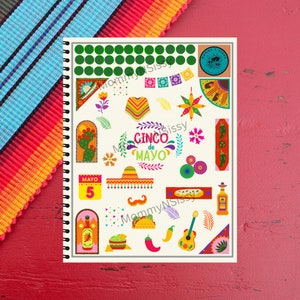 May include: A spiral-bound notebook featuring colorful Cinco de Mayo themed illustrations. Designs include a sombrero, guitar, chili peppers, and the text "Cinco de Mayo". The notebook is on a red surface with a colorful striped textile.