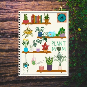 May include: A white notebook with a spiral binding features a colorful illustration of various houseplants on shelves. The text "PLANT MOM" is written in green letters with a green monstera leaf in the middle of the text.
