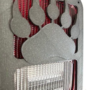 Puede incluir: Cubierta de luz trasera de plástico negro con un diseño de corte de pata de oso. La luz trasera es roja y blanca.