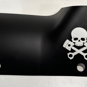 Könnte beinhalten: Schwarzes Metall-Autoteil mit einem weißen Totenkopf- und Knochenkreuz-Design mit zwei Kolben.