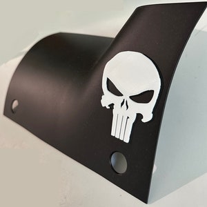Könnte beinhalten: Schwarze Metallplatte mit einem weißen Totenkopf-Motiv. Der Totenkopf hat einen weißen Umriss und schwarze Augen. Die Platte hat zwei Löcher auf der linken Seite und ein Loch auf der rechten Seite.