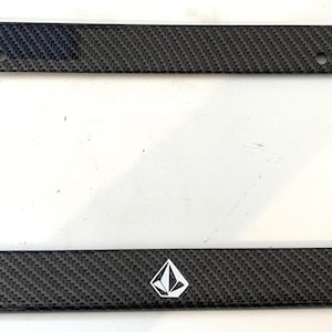 May include: Black carbon fiber license plate frame with a white diamond logo.