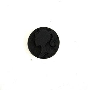 May include: A black circular button with a raised silhouette of a woman's face.