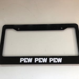 May include: Black license plate frame with the text "PEW PEW PEW" in white block letters. The frame has a rectangular shape with rounded corners and two mounting holes at the top.