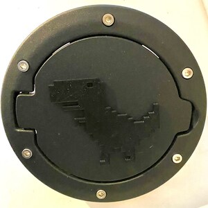 Può includere: Coperchio per tappo serbatoio benzina in plastica nera con un design di dinosauro pixelato e sei viti argentate.