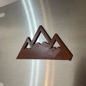 Op de afbeelding: Een bruin metalen bergketen silhouet op een geborstelde zilveren achtergrond.