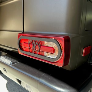 Könnte beinhalten: Eine Nahaufnahme eines schwarzen und roten Rücklichts an einem dunkelgrünen SUV. Das Rücklicht hat ein einzigartiges Design mit einem schwarzen Rahmen und einer roten Linse. Das Rücklicht ist am Heck des Fahrzeugs montiert.