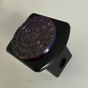 Puede incluir: Tapa de enganche de metal negro con un diseño redondo, iridiscente de calavera y brújula.